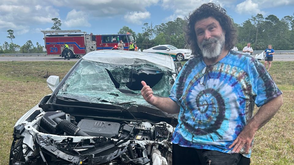 Mick Foley posing next to a destroyed car